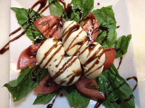 A plate of fresh basil leaves and tomato slices topped with four scoops of mozzarella drizzled with balsamic glaze.