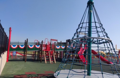 Colorful playground with climbing structure, slides, and safety surfacing under a clear blue sky.