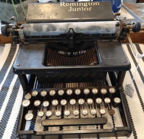 A vintage Remington Junior typewriter with a black body and white keys, displayed on a textured surface.