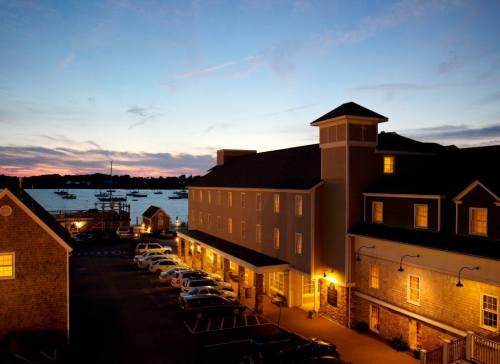 A hotel by the water at sunset, with boats in the background and cars parked in front.