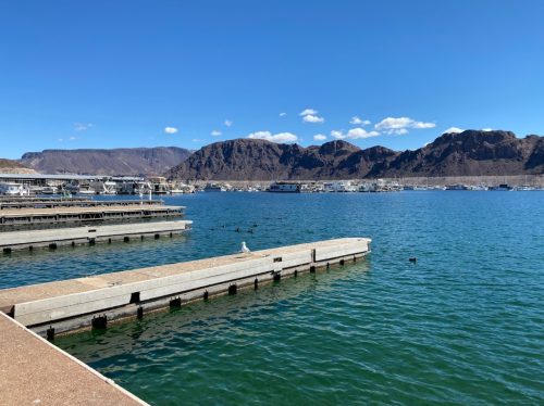 A serene marina with docks on a clear blue lake, surrounded by mountains under a bright sky.