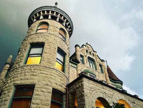 A tall, stone castle with turrets and large windows, set against a moody sky.