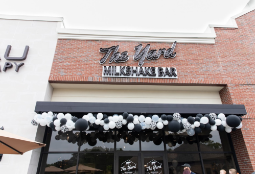 Exterior of The Yard Milkshake Bar, featuring a sign and a festive balloon arch in black and white.