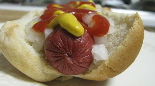 A close-up of a hot dog in a bun, topped with ketchup, mustard, and chopped onions.