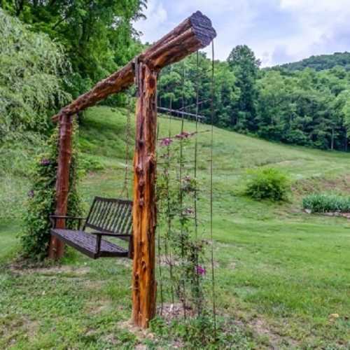 A rustic wooden swing hangs from a sturdy frame, surrounded by lush green grass and trees in a serene outdoor setting.