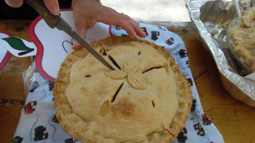 A hand using a knife to cut into a decorative pie on a colorful tablecloth.