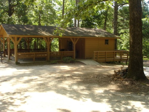 A wooden cabin surrounded by trees, featuring a porch and a gravel path leading to the entrance.