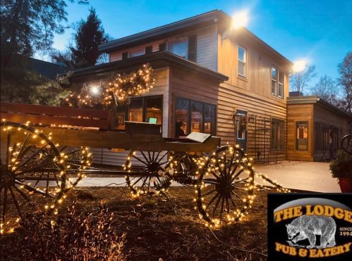 A cozy lodge with warm lights, featuring a wooden wagon decorated with string lights in front of the entrance.