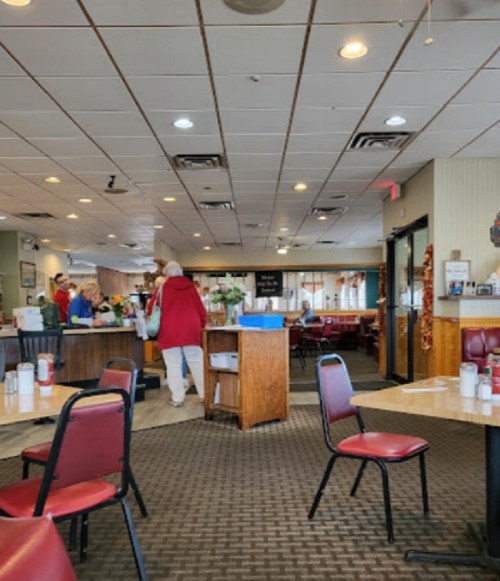Interior of a diner with red chairs, wooden tables, and patrons at the counter. Brightly lit and welcoming atmosphere.
