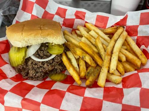 A sandwich with ground beef, pickles, and onions, served with a side of golden French fries on red and white checkered paper.