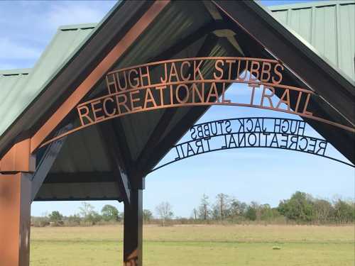 Sign for Hugh Jack Stubbs Recreational Trail under a green roof, with open grassy area in the background.