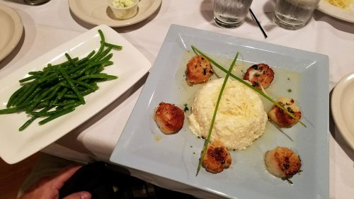 A plate of scallops arranged around a mound of rice, garnished with green onions, alongside a side of green beans.
