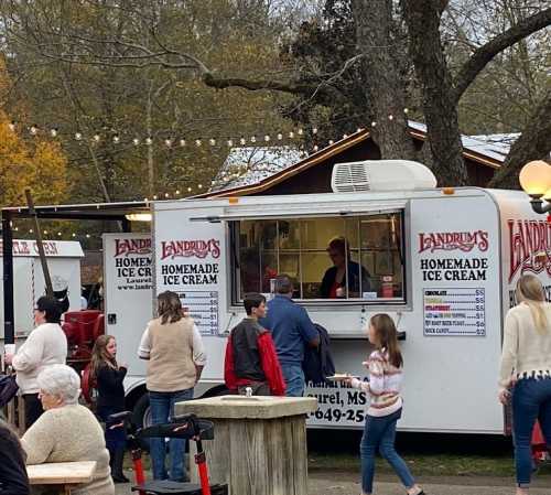 A busy ice cream truck with people ordering and enjoying treats in a festive outdoor setting.