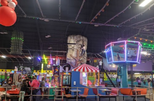 A vibrant indoor amusement center with climbing wall, arcade games, and colorful decorations. Families enjoy various activities.
