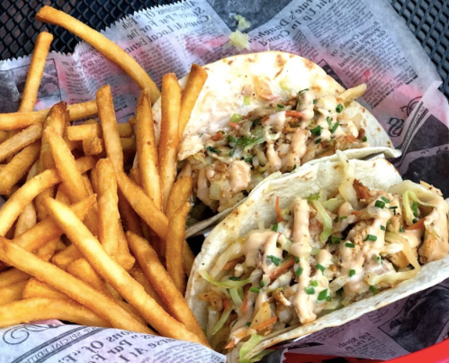 Two tacos with shredded cabbage and sauce, served with a side of golden French fries in a basket.
