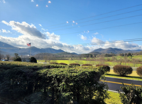 A scenic view of mountains and fields under a blue sky, with an American flag and greenery in the foreground.