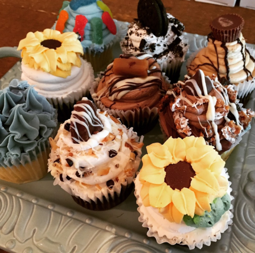 A variety of colorful cupcakes decorated with flowers, chocolate, and drizzles, arranged on a decorative platter.