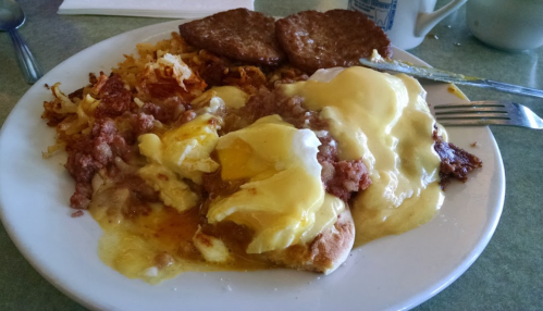 A plate of breakfast featuring eggs, sausage, cheese, hash browns, and two sausage patties.
