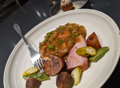 A plate of sliced meat with a savory sauce, accompanied by roasted potatoes and green vegetables.
