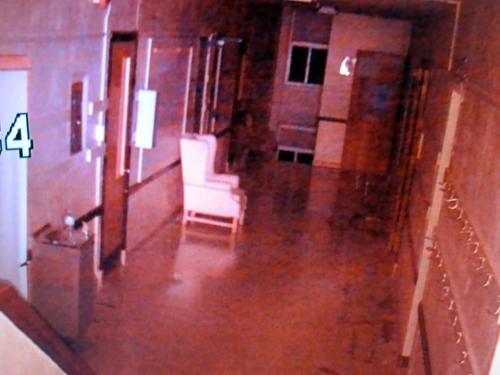 Dimly lit hallway with a single chair at the end, featuring a reflective floor and empty walls.