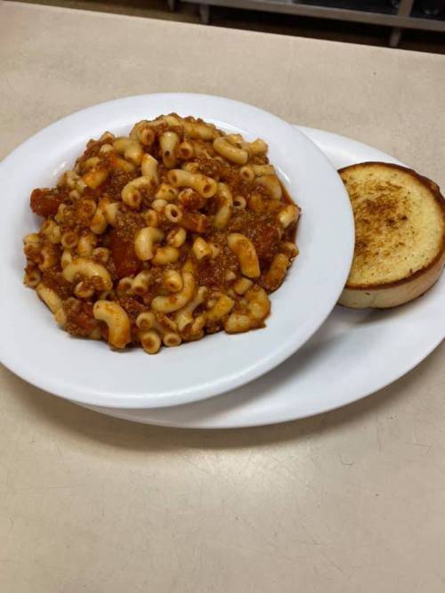 A plate of macaroni with meat sauce and a slice of toasted bread on the side.