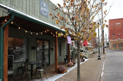 A cozy storefront with outdoor seating, string lights, and autumn leaves lining the sidewalk on a quiet street.