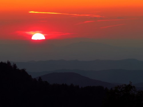 A vibrant sunset over layered mountains, with hues of orange and red illuminating the sky.