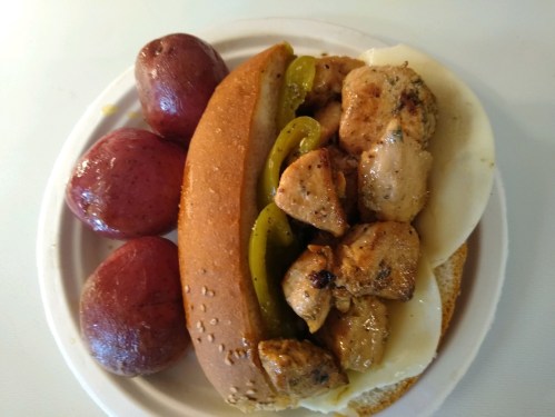 A plate with a sandwich filled with grilled chicken, peppers, and cheese, alongside two red potatoes.