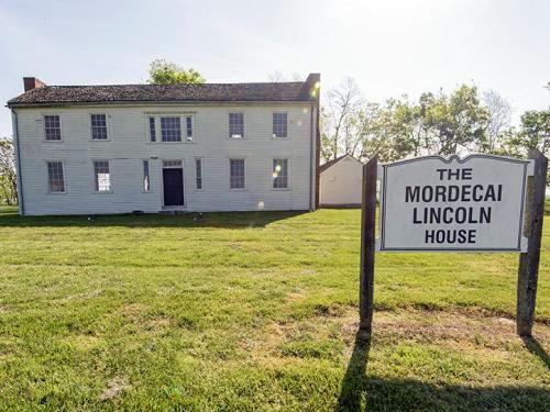 Historic Mordecai Lincoln House with a sign in front, set on a grassy area under a clear sky.