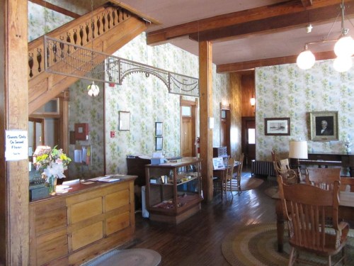 A cozy interior of a vintage building featuring wooden furniture, floral wallpaper, and a staircase.