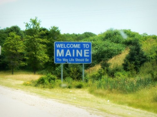 A blue welcome sign for Maine surrounded by greenery, stating, "The Way Life Should Be."