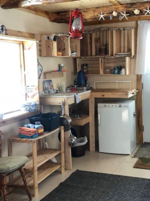 Cozy kitchen with wooden shelves, a lantern, and a small fridge, featuring a rustic, homey atmosphere.