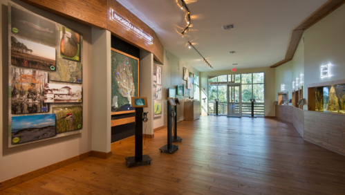Interior view of a nature center with wooden floors, informational displays, and large windows letting in natural light.