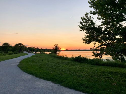 A serene sunset over a lake, with a winding path and lush greenery along the shore.