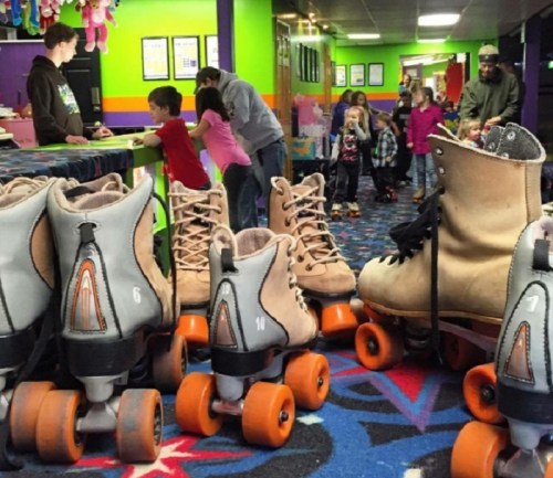 A colorful roller skating rink with skates in the foreground and children skating and socializing in the background.