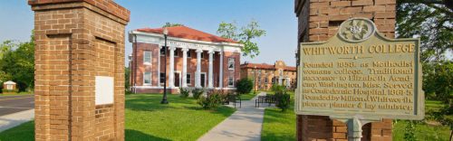 Historic Whitworth College building with columns, surrounded by green lawns and a sign detailing its founding.