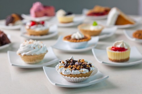 A variety of desserts on white plates, including mini pies, cupcakes, and cream-topped treats.