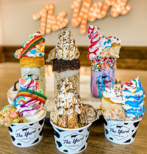 A colorful display of ice cream treats, including milkshakes and cones, from The Yard, with a bright sign in the background.
