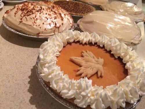 A variety of pies, including a pumpkin pie with whipped cream and a decorative crust, displayed on a countertop.