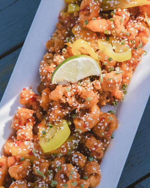 A platter of crispy, orange-glazed shrimp garnished with lime, yellow peppers, and sesame seeds.