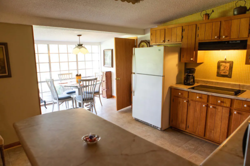 A cozy kitchen with wooden cabinets, a white fridge, and a dining area with a table and chairs in natural light.