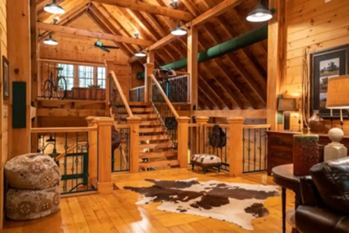 Cozy wooden interior of a cabin with a staircase, rustic decor, and warm lighting.