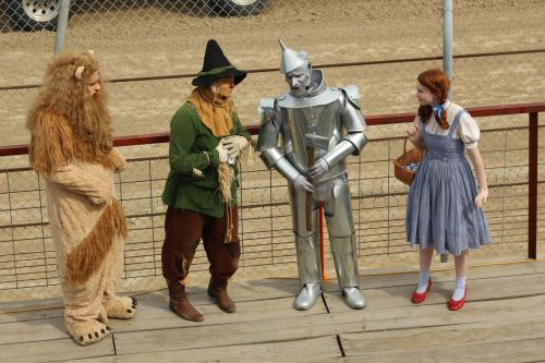 Four characters from "The Wizard of Oz" stand together: the Cowardly Lion, Scarecrow, Tin Man, and Dorothy.