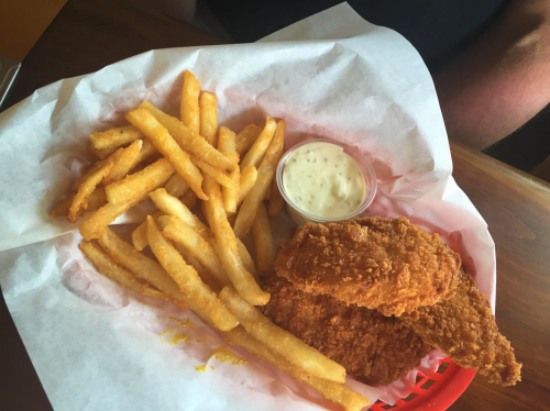 A basket of golden fries and three crispy chicken tenders with a side of dipping sauce.