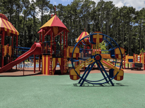 Colorful playground with a slide and a Ferris wheel, surrounded by trees and blue sky.