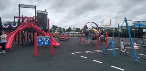 A playground with slides, climbing structures, and children playing, set against a cloudy sky.