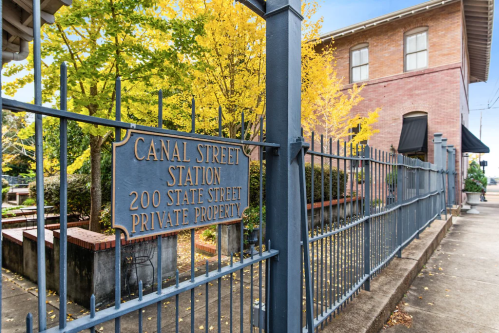 Sign for Canal Street Station, featuring a brick building and vibrant yellow trees in the background. Private property notice.