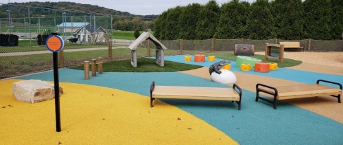 Colorful playground with various play structures, including a slide, climbing area, and benches on a rubber surface.