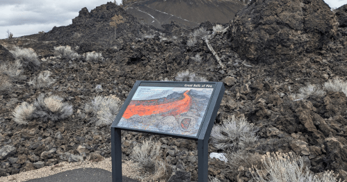 A sign displaying information about the Great Rift of Fire, surrounded by volcanic rock and sparse vegetation.