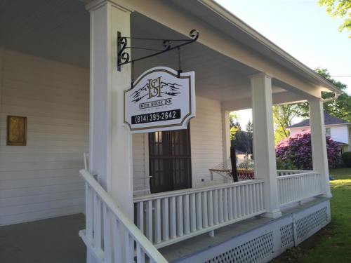 A white house with a porch and a sign hanging that reads "S&F" with a phone number. Greenery and flowers in the background.